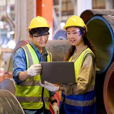 NEUI aluminum design specialists in safety gear inspecting a large metal pipe with a laptop